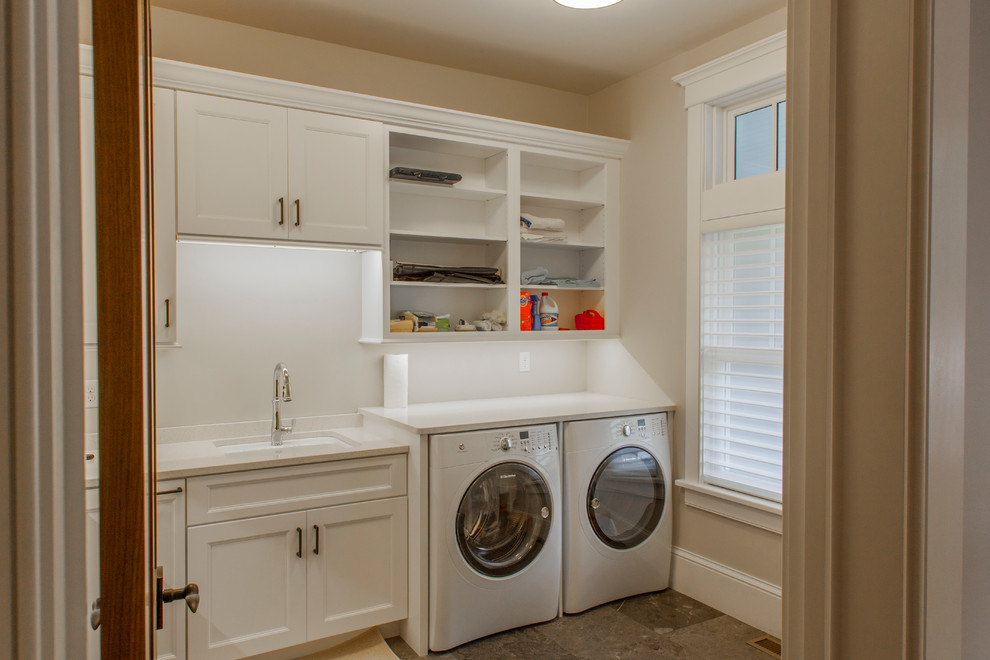 Inspiration för mellanstora klassiska l-formade tvättstugor enbart för tvätt, med en undermonterad diskho, släta luckor, vita skåp, bänkskiva i kvarts, klinkergolv i porslin och en tvättmaskin och torktumlare bredvid varandra