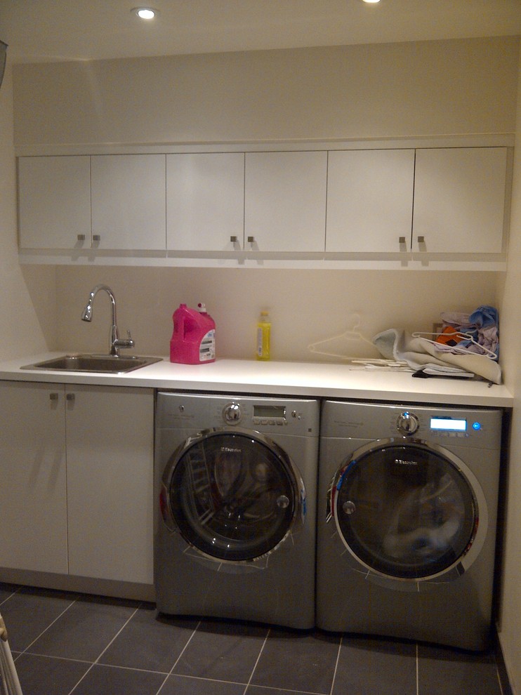 Immagine di una lavanderia multiuso moderna di medie dimensioni con lavello da incasso, ante lisce, ante bianche, top in laminato, pareti beige, pavimento con piastrelle in ceramica e lavatrice e asciugatrice affiancate