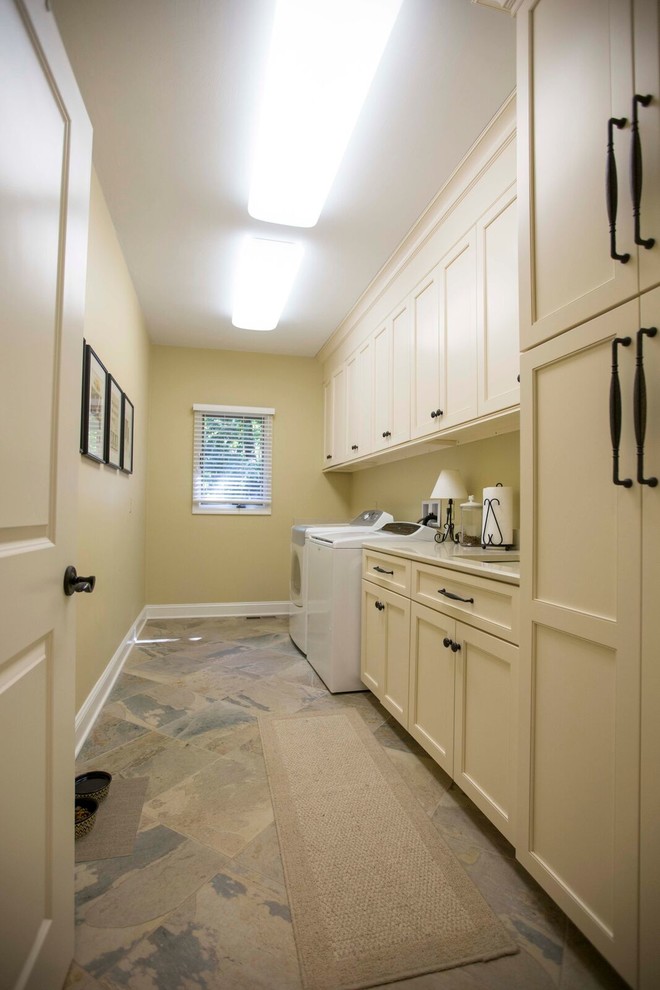 This is an example of a large traditional single-wall separated utility room in Other with a submerged sink, recessed-panel cabinets, white cabinets, composite countertops, beige walls, slate flooring, a side by side washer and dryer and brown floors.