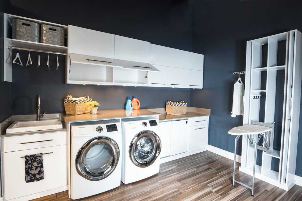 Mid-sized transitional single-wall medium tone wood floor and brown floor laundry room photo in Phoenix with a drop-in sink, flat-panel cabinets, white cabinets, solid surface countertops, black walls and a side-by-side washer/dryer
