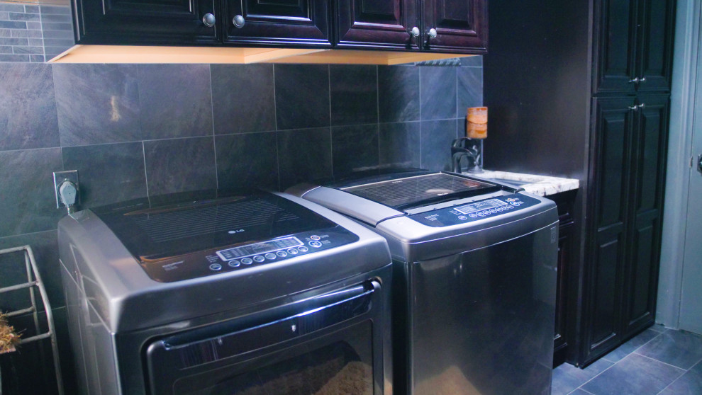 Bild på en stor flerfärgade parallell flerfärgat tvättstuga enbart för tvätt, med luckor med profilerade fronter, bruna skåp, granitbänkskiva, grått stänkskydd, grå väggar, en tvättmaskin och torktumlare bredvid varandra och grått golv