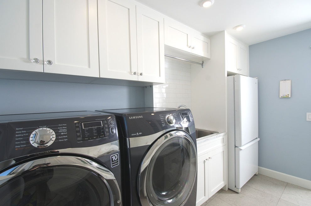 Klassisk inredning av en parallell tvättstuga enbart för tvätt, med en enkel diskho, släta luckor, vita skåp, laminatbänkskiva, blå väggar, kalkstensgolv och en tvättmaskin och torktumlare bredvid varandra