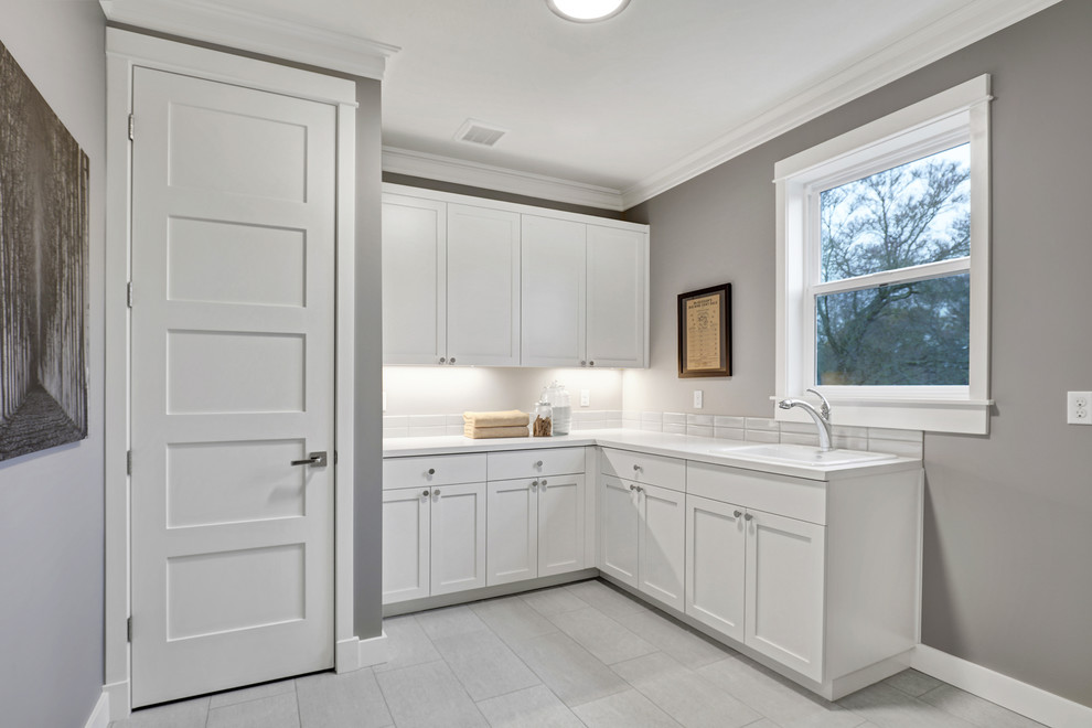 Inspiration for a craftsman l-shaped porcelain tile dedicated laundry room remodel in Seattle with recessed-panel cabinets, white cabinets, beige walls, a side-by-side washer/dryer, an utility sink and solid surface countertops
