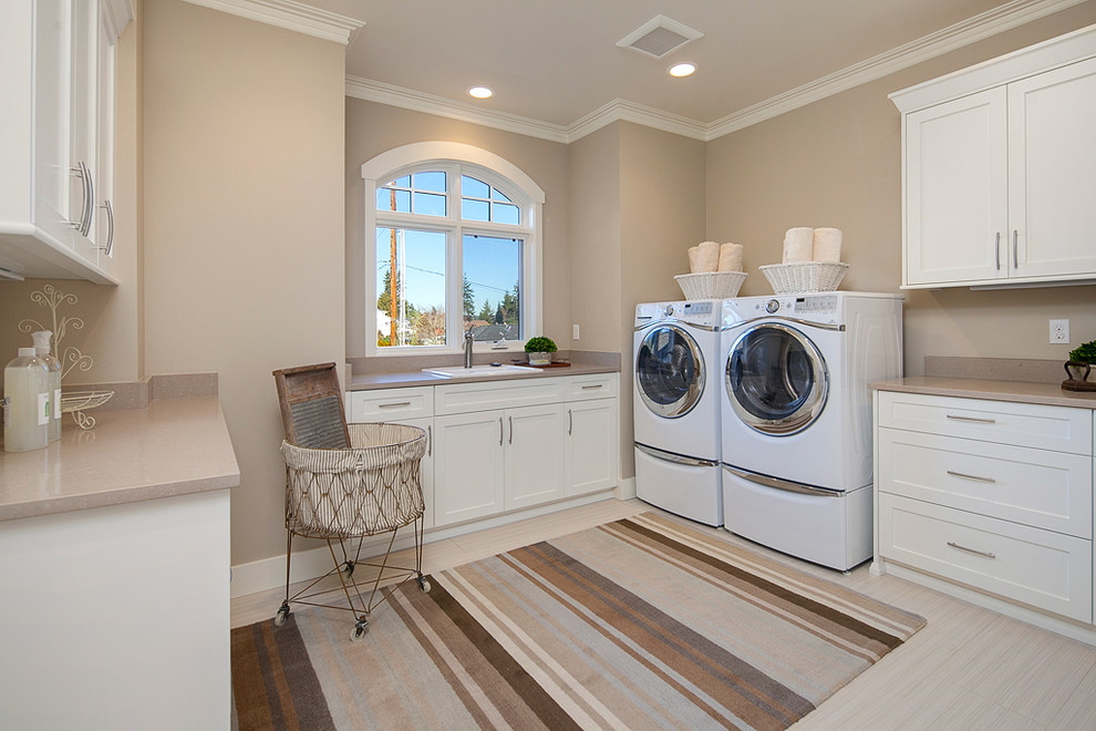 Trendy u-shaped porcelain tile dedicated laundry room photo in Seattle with a side-by-side washer/dryer, a drop-in sink, recessed-panel cabinets, white cabinets, quartz countertops and beige walls