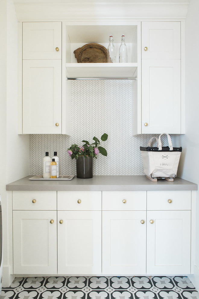 Klassisk inredning av en mellanstor grå linjär grått tvättstuga enbart för tvätt, med luckor med infälld panel, vita skåp, bänkskiva i kvarts, vita väggar, klinkergolv i keramik och svart golv