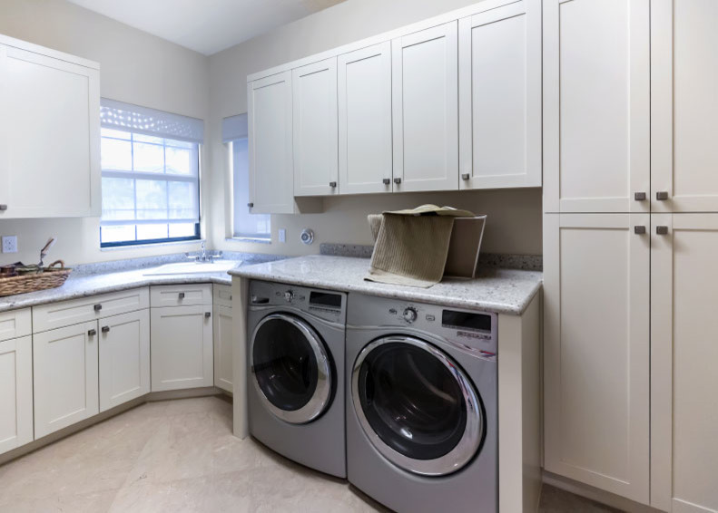 This is an example of a medium sized traditional l-shaped utility room in New York with an utility sink, shaker cabinets, white cabinets, beige walls and a side by side washer and dryer.