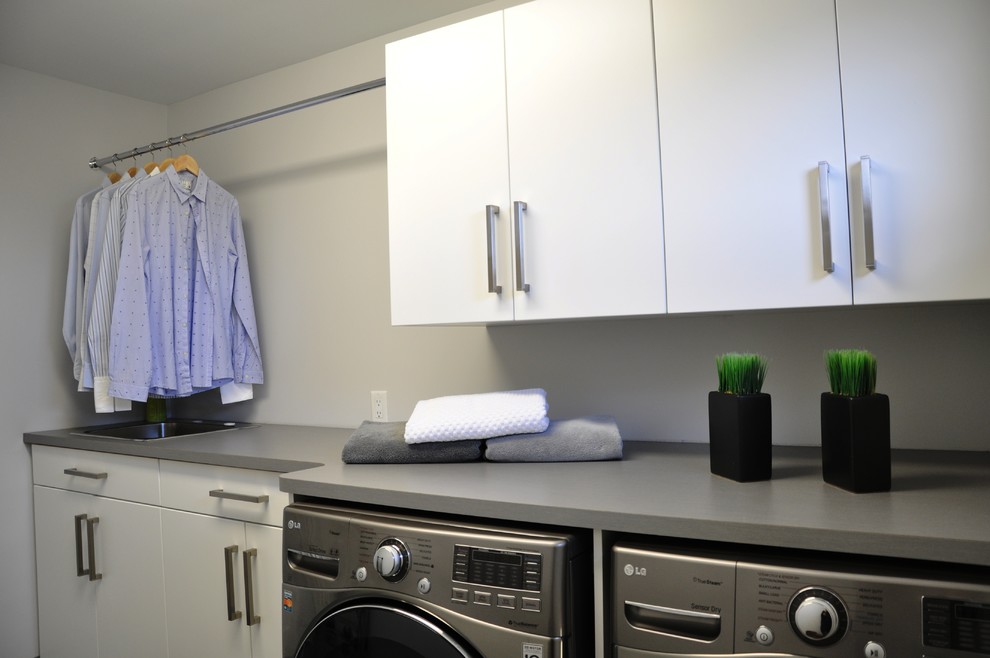 Idéer för att renovera en mellanstor funkis linjär tvättstuga enbart för tvätt, med en nedsänkt diskho, släta luckor, vita skåp, bänkskiva i kvarts, grå väggar och en tvättmaskin och torktumlare bredvid varandra