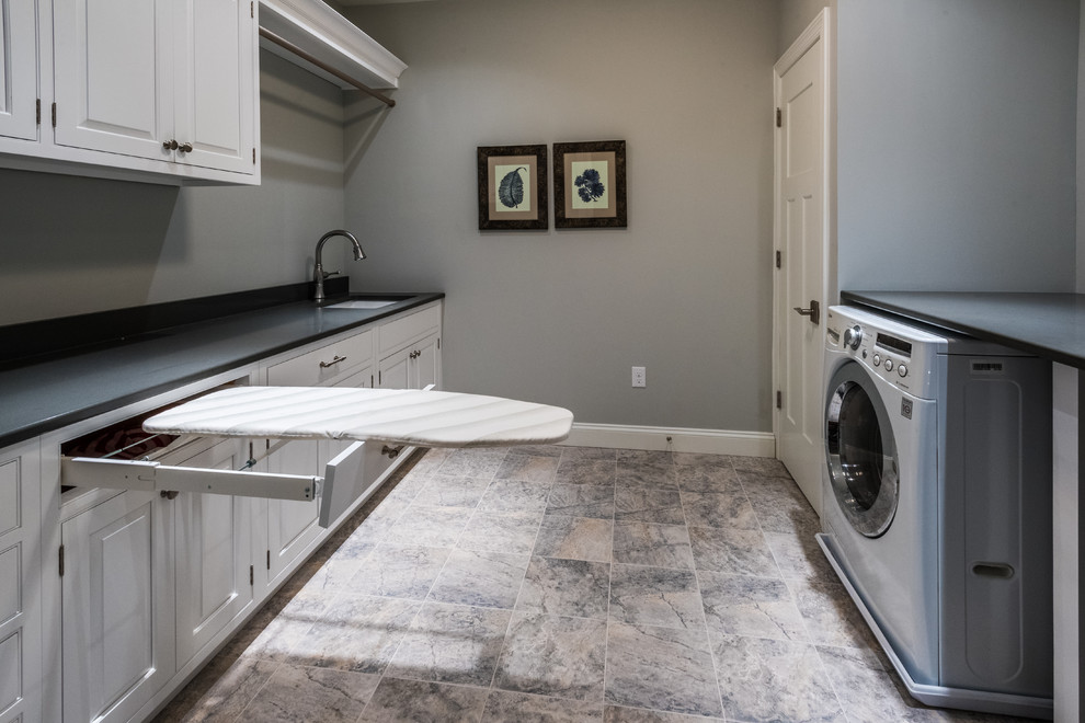 Klassisk inredning av en mellanstor parallell tvättstuga enbart för tvätt, med en undermonterad diskho, vita skåp, granitbänkskiva, grå väggar, klinkergolv i keramik, en tvättmaskin och torktumlare bredvid varandra och luckor med upphöjd panel