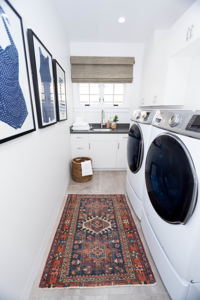 Klassisk inredning av en liten l-formad tvättstuga enbart för tvätt, med en undermonterad diskho, släta luckor, vita skåp, vita väggar, en tvättmaskin och torktumlare bredvid varandra och beiget golv