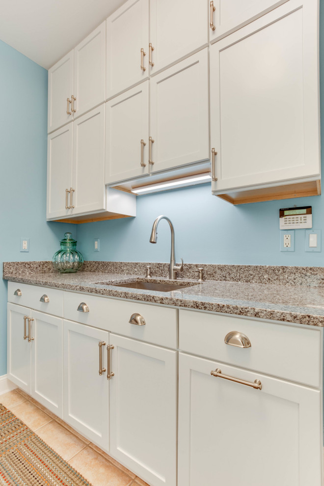 Example of a mid-sized transitional galley dedicated laundry room design in Baltimore with an undermount sink, shaker cabinets, white cabinets, granite countertops, blue walls and a stacked washer/dryer