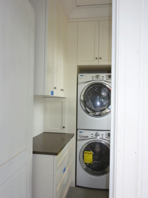 Moderner Hauswirtschaftsraum in L-Form mit Waschmaschinenschrank, Schrankfronten im Shaker-Stil und Waschmaschine und Trockner gestapelt in New York