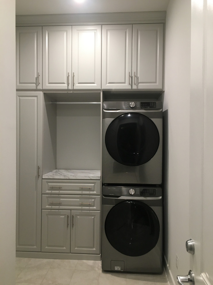 Design ideas for a small modern single-wall separated utility room in DC Metro with raised-panel cabinets, grey cabinets, laminate countertops, grey walls, porcelain flooring, a stacked washer and dryer and multicoloured worktops.