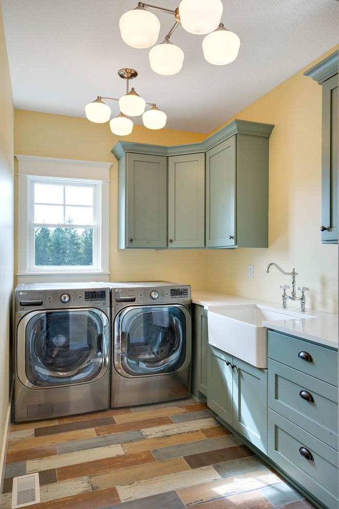 Inredning av en lantlig l-formad tvättstuga, med en rustik diskho, skåp i shakerstil, blå skåp, marmorbänkskiva, gula väggar och en tvättmaskin och torktumlare bredvid varandra