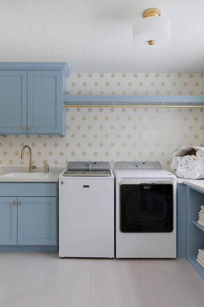 Klassisk inredning av en l-formad tvättstuga enbart för tvätt, med en nedsänkt diskho, skåp i shakerstil, blå skåp, laminatbänkskiva, en tvättmaskin och torktumlare bredvid varandra, flerfärgade väggar och beiget golv