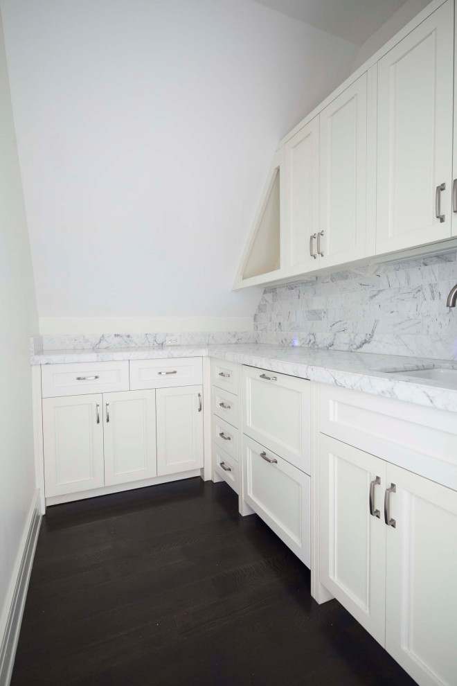 Idéer för en stor modern grå l-formad tvättstuga enbart för tvätt, med en undermonterad diskho, luckor med profilerade fronter, vita skåp, marmorbänkskiva, vita väggar, mörkt trägolv och en tvättmaskin och torktumlare bredvid varandra