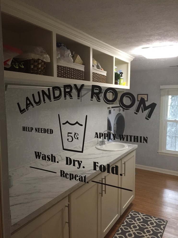 Example of a mid-sized trendy l-shaped light wood floor dedicated laundry room design in Atlanta with a drop-in sink, shaker cabinets, beige cabinets, granite countertops, gray walls and a side-by-side washer/dryer
