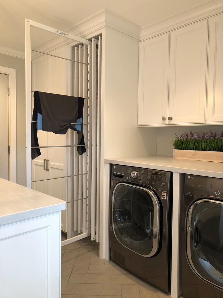 Inspiration for a medium sized traditional galley utility room in Milwaukee with a belfast sink, recessed-panel cabinets, white cabinets, grey walls, ceramic flooring, a concealed washer and dryer, brown floors and grey worktops.