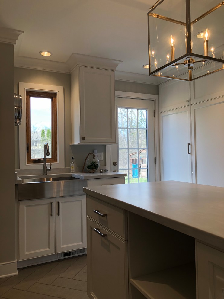 Inspiration for a mid-sized timeless galley ceramic tile and brown floor utility room remodel in Milwaukee with recessed-panel cabinets, white cabinets, a farmhouse sink, gray walls, a concealed washer/dryer and gray countertops