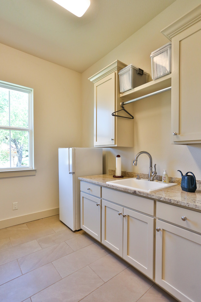 Inspiration for a mid-sized timeless galley ceramic tile and beige floor dedicated laundry room remodel in Austin with a farmhouse sink, recessed-panel cabinets, beige cabinets, granite countertops, beige walls, a side-by-side washer/dryer and multicolored countertops
