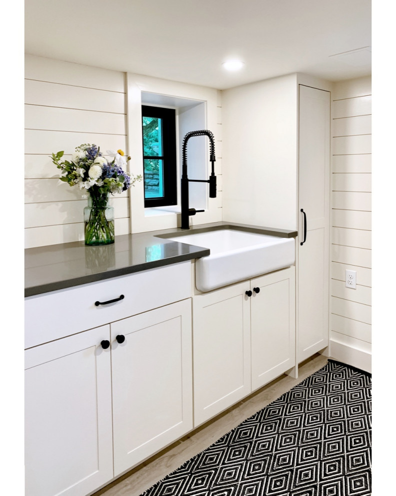 Exempel på en mellanstor lantlig grå l-formad grått tvättstuga enbart för tvätt, med en rustik diskho, skåp i shakerstil, vita skåp, bänkskiva i kvarts, vita väggar, vinylgolv, en tvättmaskin och torktumlare bredvid varandra och grått golv