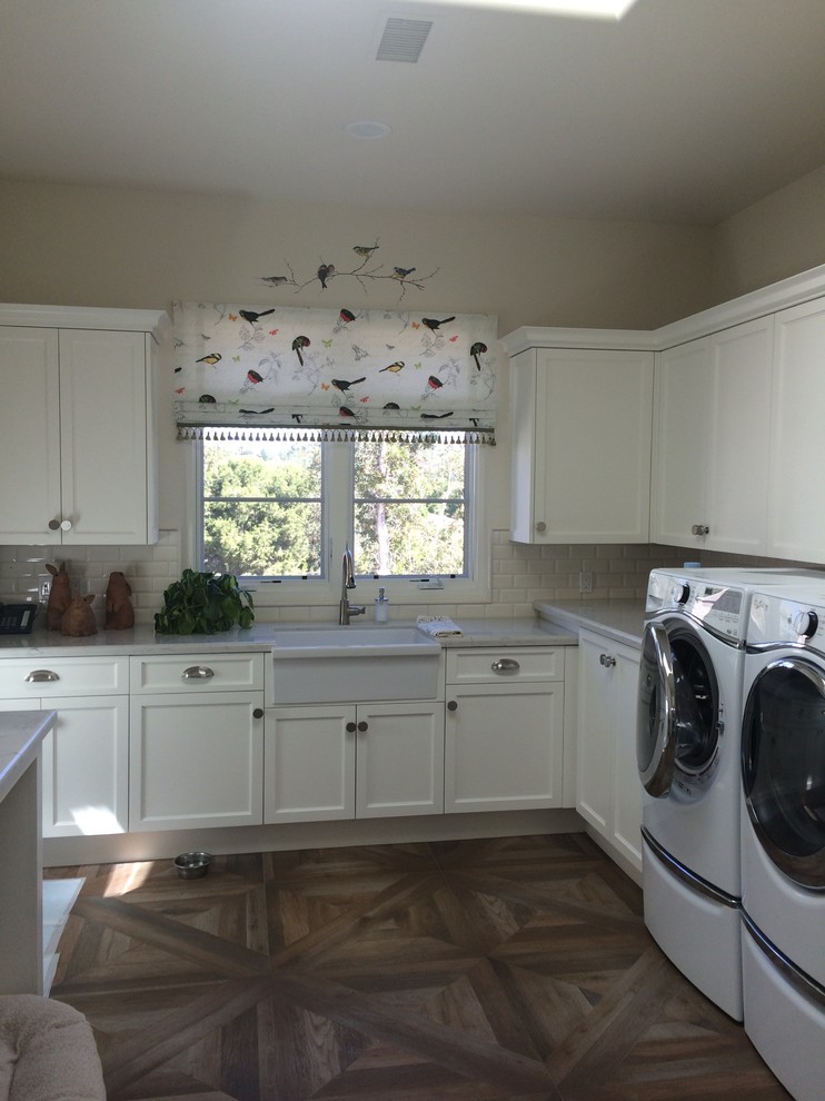 Inspiration for a medium sized traditional l-shaped utility room in San Diego with a belfast sink, shaker cabinets, white cabinets, composite countertops, beige walls, medium hardwood flooring and a side by side washer and dryer.