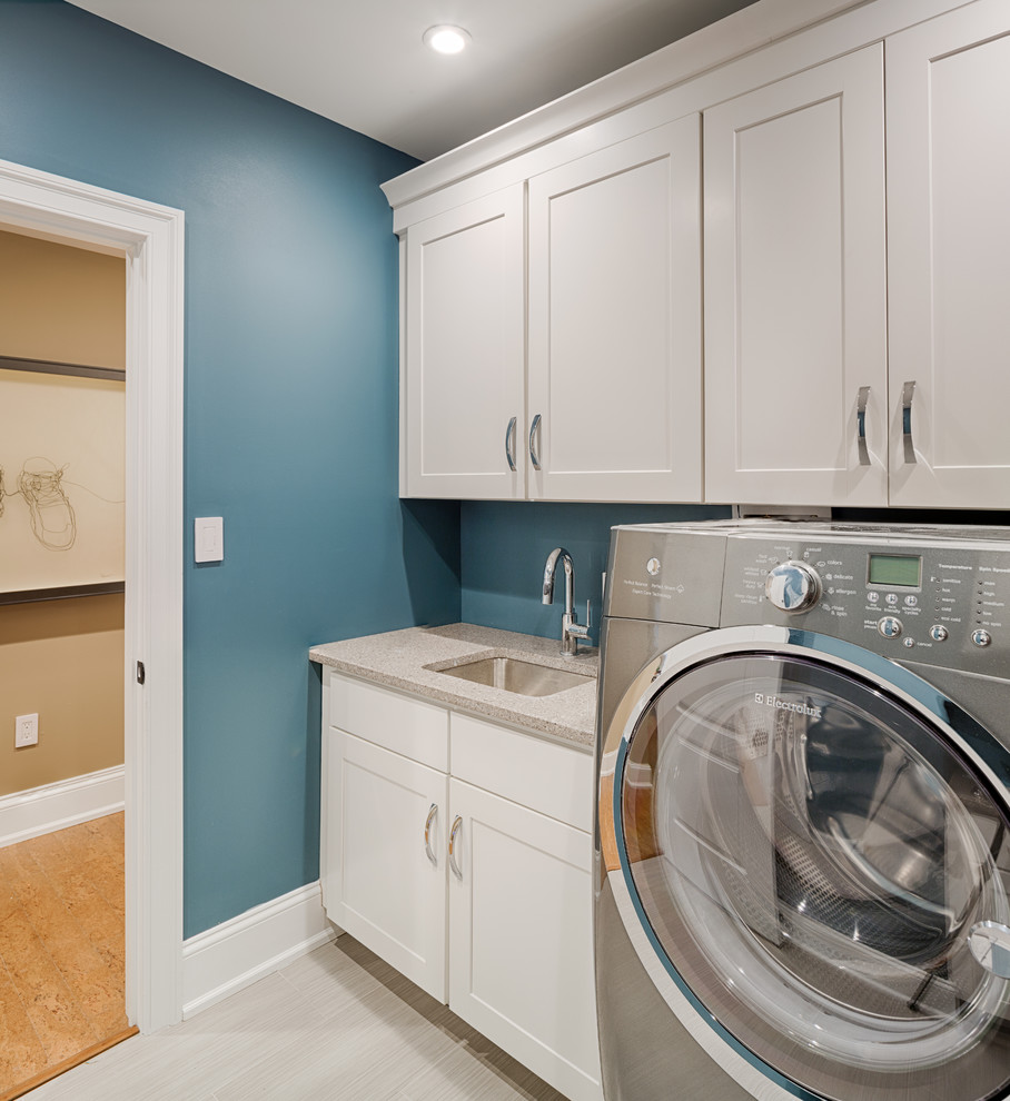 Diseño de cuarto de lavado lineal clásico renovado con fregadero bajoencimera, armarios con paneles empotrados, puertas de armario blancas, encimera de acrílico, paredes azules y lavadora y secadora juntas