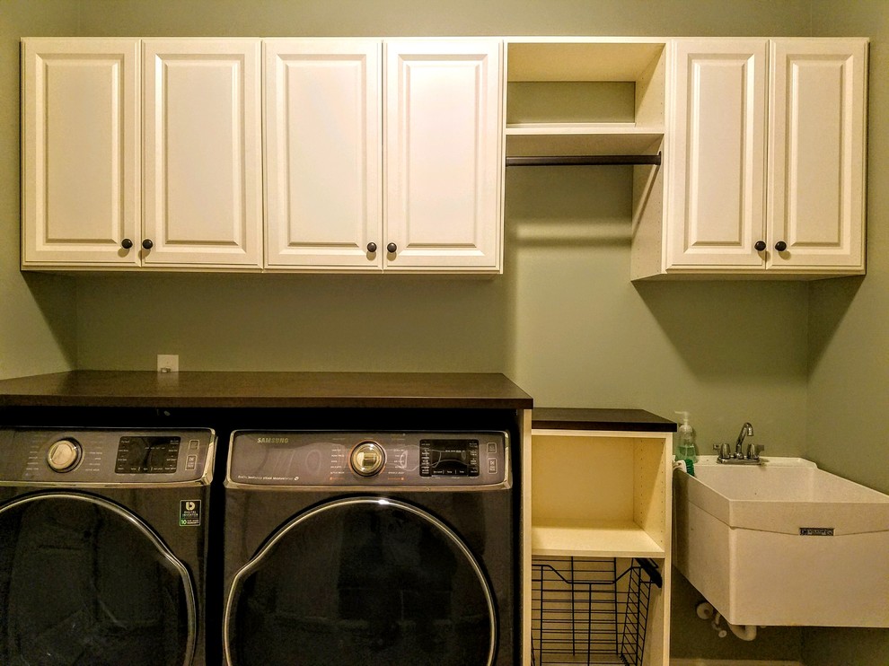 Exempel på en mellanstor klassisk bruna parallell brunt tvättstuga enbart för tvätt, med en allbänk, luckor med upphöjd panel, vita skåp, laminatbänkskiva, en tvättmaskin och torktumlare bredvid varandra och gröna väggar