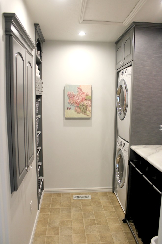 ソルトレイクシティにある低価格の小さなトランジショナルスタイルのおしゃれな洗濯室 (ll型、レイズドパネル扉のキャビネット、グレーのキャビネット、ラミネートカウンター、白い壁、リノリウムの床、上下配置の洗濯機・乾燥機) の写真