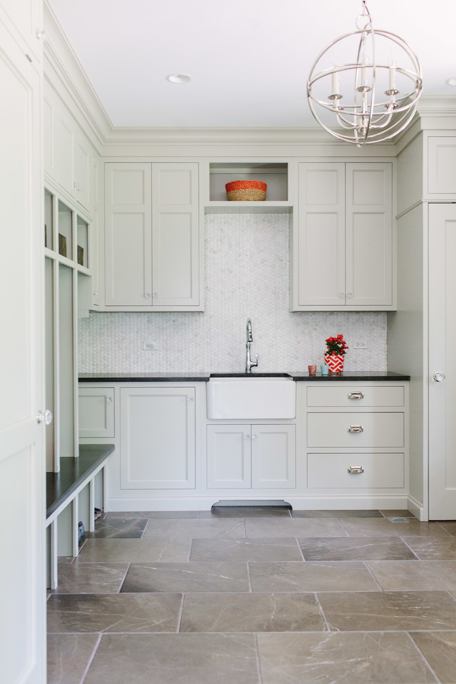 Example of a large transitional l-shaped marble floor dedicated laundry room design in Chicago with a farmhouse sink, recessed-panel cabinets, white cabinets, solid surface countertops and white walls