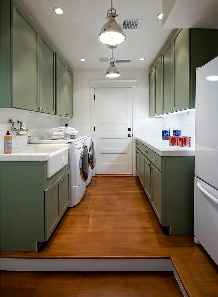 Zweizeilige, Große Klassische Waschküche mit Landhausspüle, Schrankfronten im Shaker-Stil, weißer Wandfarbe, braunem Holzboden, Waschmaschine und Trockner nebeneinander, grünen Schränken, Marmor-Arbeitsplatte und weißer Arbeitsplatte in Los Angeles
