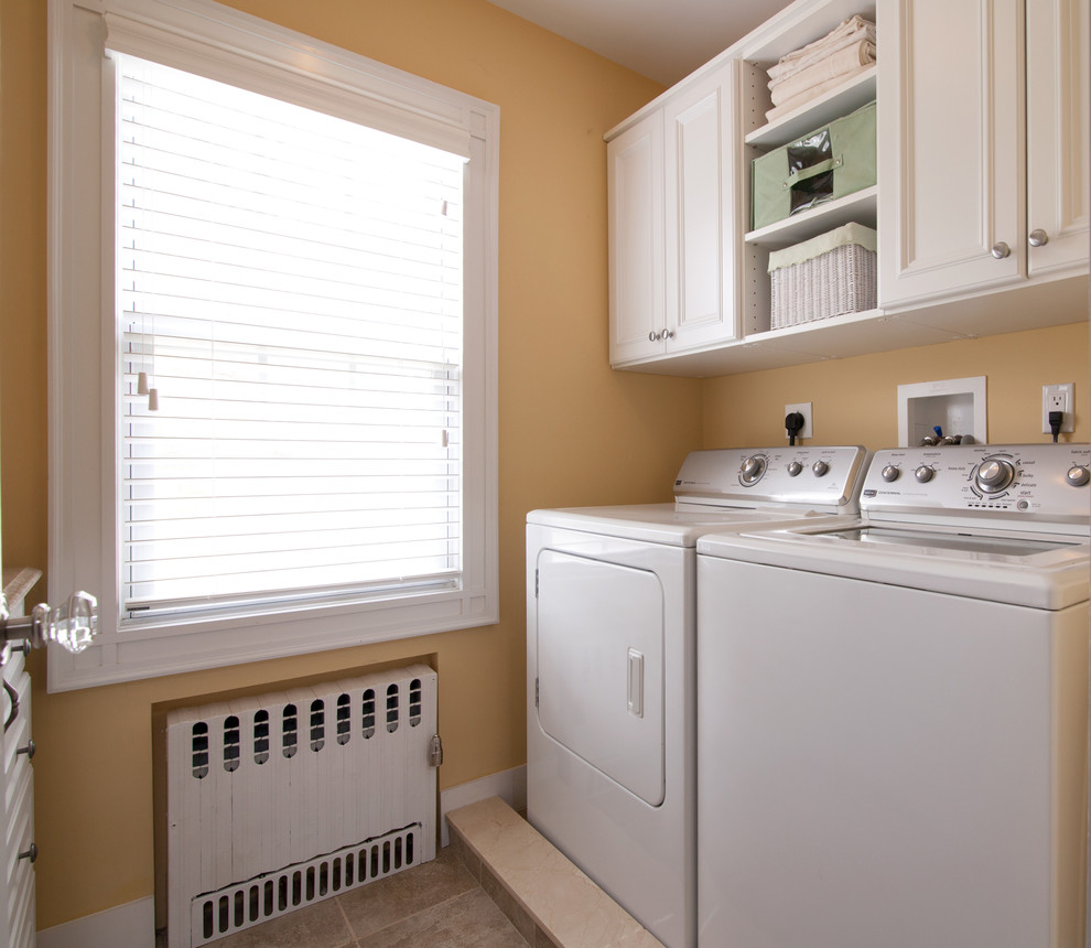Klassisk inredning av en mellanstor parallell tvättstuga enbart för tvätt, med luckor med infälld panel, vita skåp, granitbänkskiva, orange väggar och en tvättmaskin och torktumlare bredvid varandra