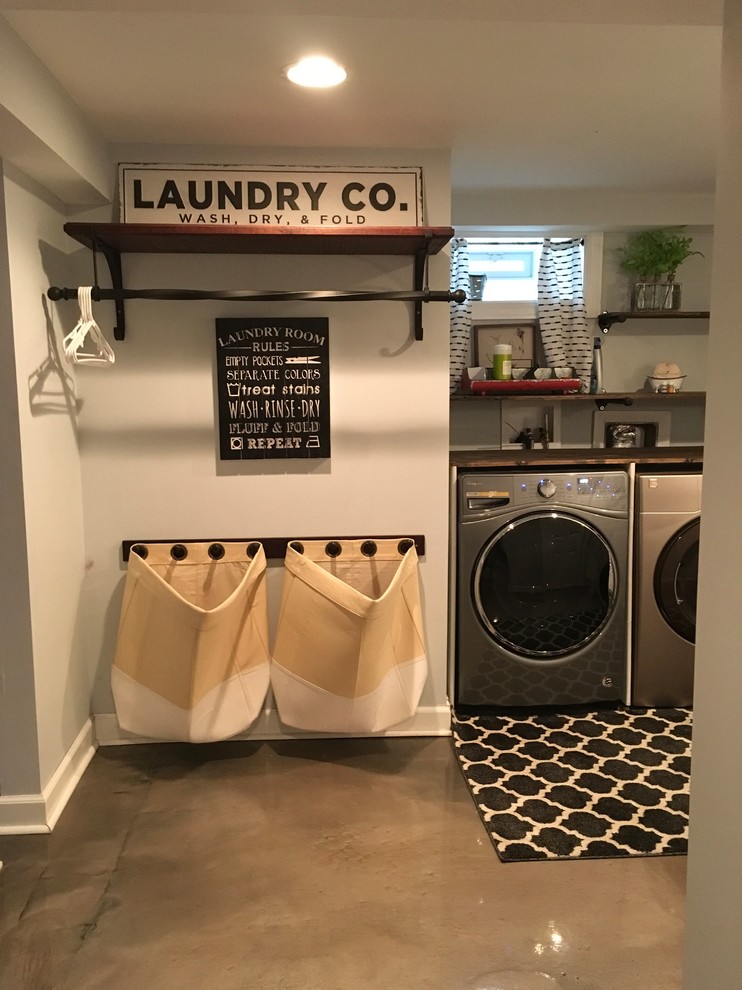 Bild på en mellanstor lantlig tvättstuga enbart för tvätt, med en undermonterad diskho, träbänkskiva, grå väggar, betonggolv, en tvättmaskin och torktumlare bredvid varandra och grått golv