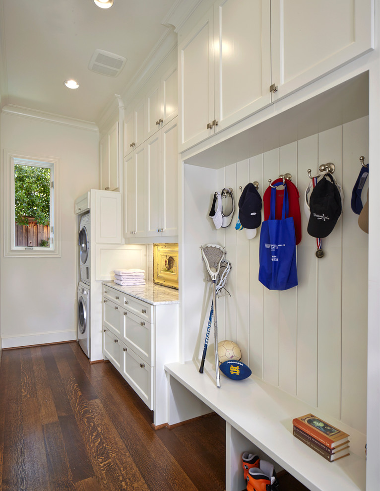 Photo of a small classic single-wall utility room in Dallas with shaker cabinets, white cabinets, marble worktops, white walls, a stacked washer and dryer, dark hardwood flooring, brown floors and white worktops.