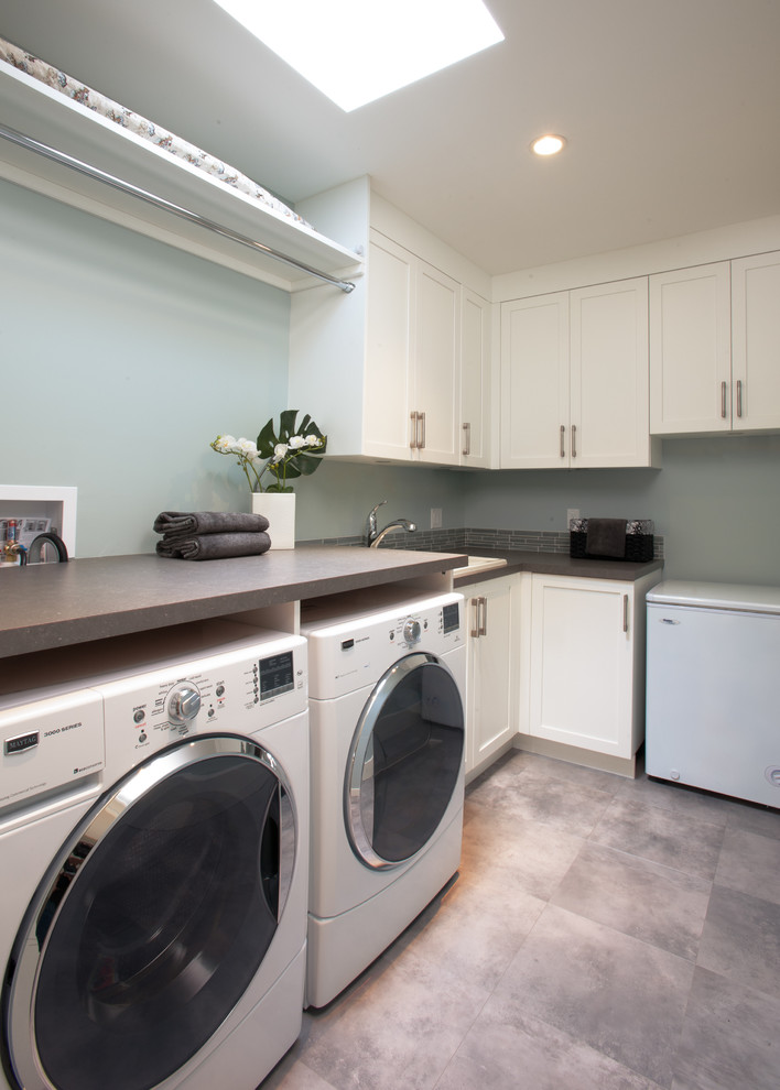 Ejemplo de cuarto de lavado en L clásico renovado de tamaño medio con armarios con paneles empotrados, puertas de armario blancas, encimera de laminado, paredes grises y lavadora y secadora juntas