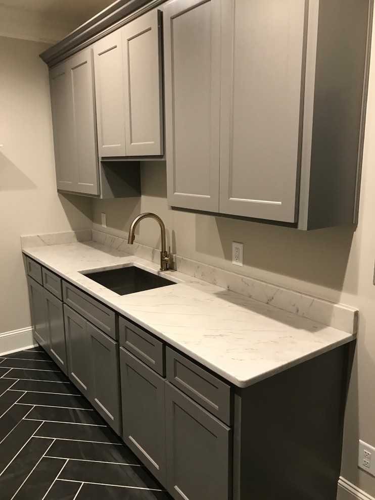 Photo of a medium sized traditional galley utility room in Raleigh with a submerged sink, shaker cabinets, grey cabinets, engineered stone countertops, grey walls, slate flooring, a side by side washer and dryer and black floors.