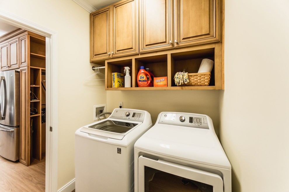 Small elegant galley laminate floor and brown floor laundry room photo in Charleston with raised-panel cabinets, medium tone wood cabinets, beige walls and a side-by-side washer/dryer