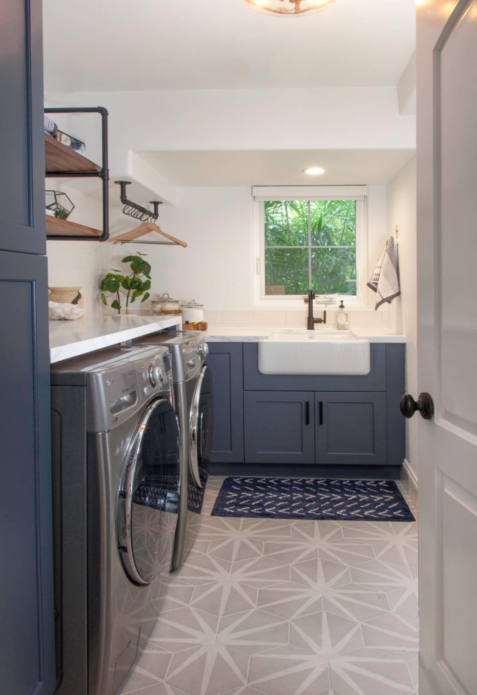 Medium sized nautical l-shaped separated utility room in Denver with a belfast sink, recessed-panel cabinets, blue cabinets, engineered stone countertops, white walls, porcelain flooring, a side by side washer and dryer, grey floors and white worktops.