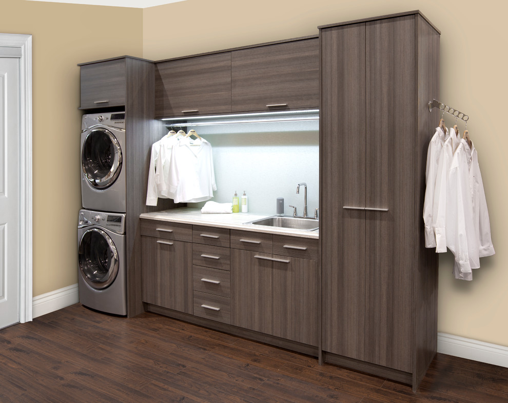 Mid-sized trendy single-wall dark wood floor utility room photo in Toronto with flat-panel cabinets, beige walls, a stacked washer/dryer and gray cabinets
