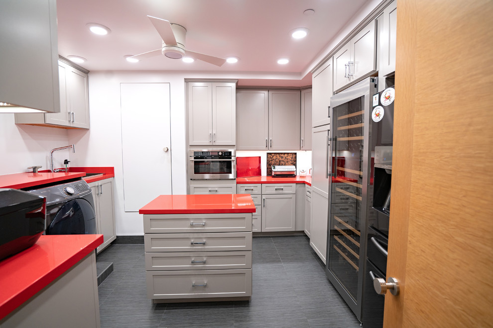 Modern inredning av ett röd linjärt rött grovkök, med en nedsänkt diskho, grå skåp, vita väggar, en tvättmaskin och torktumlare bredvid varandra, grått golv och skåp i shakerstil