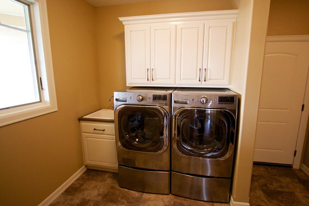 Immagine di una lavanderia multiuso di medie dimensioni con ante con bugna sagomata, ante bianche, top in laminato e lavatrice e asciugatrice affiancate