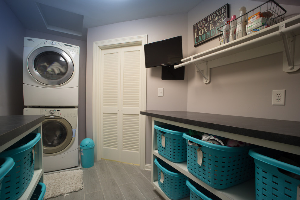 Ejemplo de cuarto de lavado de galera clásico de tamaño medio con armarios abiertos, encimera de acrílico, paredes púrpuras, suelo vinílico, lavadora y secadora apiladas y suelo gris