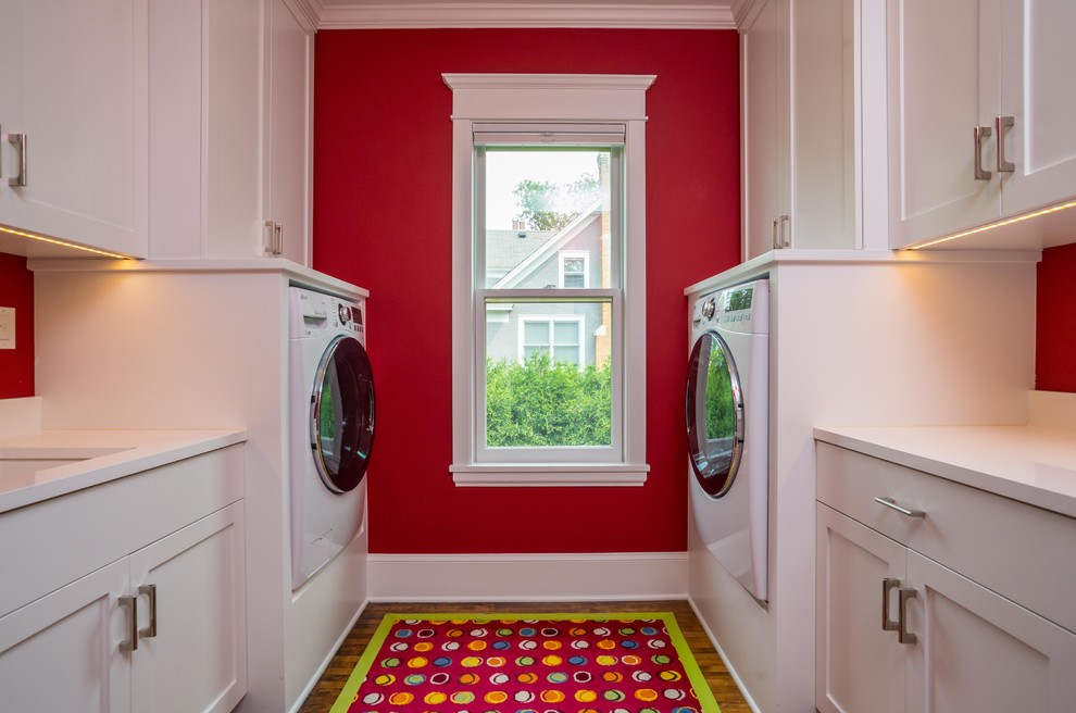 Cette image montre une buanderie parallèle traditionnelle de taille moyenne avec un placard à porte shaker, des portes de placard blanches, un plan de travail en quartz modifié, un mur rouge et un sol en bois brun.