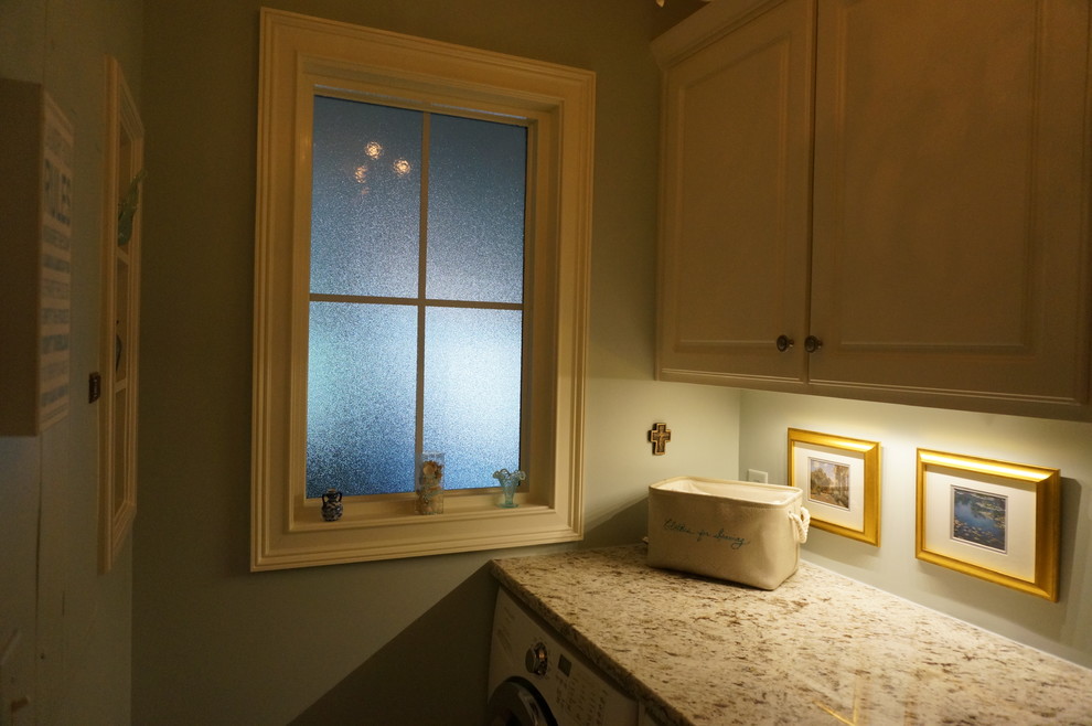 Exempel på en liten klassisk parallell tvättstuga enbart för tvätt, med luckor med upphöjd panel, vita skåp, granitbänkskiva, blå väggar och en tvättmaskin och torktumlare bredvid varandra