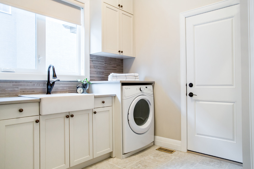 Ejemplo de cuarto de lavado lineal tradicional de tamaño medio con fregadero sobremueble, armarios con rebordes decorativos, puertas de armario blancas, encimera de cuarzo compacto y suelo gris
