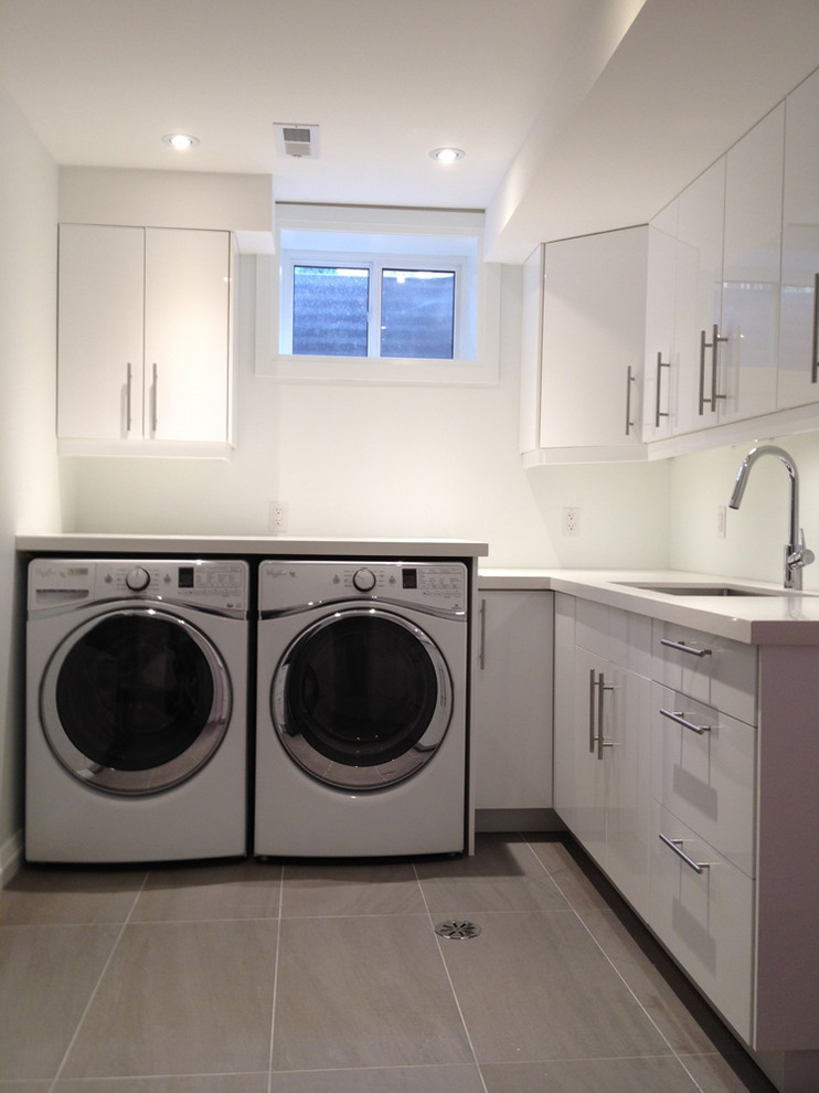 Große Moderne Waschküche in L-Form mit Unterbauwaschbecken, flächenbündigen Schrankfronten, weißen Schränken, Quarzwerkstein-Arbeitsplatte, weißer Wandfarbe, Keramikboden und Waschmaschine und Trockner nebeneinander in Toronto