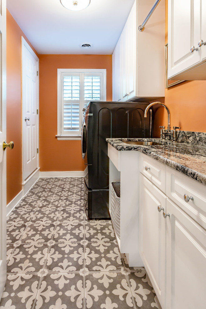 Idéer för att renovera en mellanstor flerfärgade parallell flerfärgat tvättstuga enbart för tvätt, med en undermonterad diskho, vita skåp, granitbänkskiva, orange väggar, en tvättmaskin och torktumlare bredvid varandra och flerfärgat golv