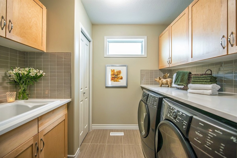 This is an example of a traditional galley utility room in Edmonton with a built-in sink, shaker cabinets, light wood cabinets, a side by side washer and dryer, brown floors and beige walls.