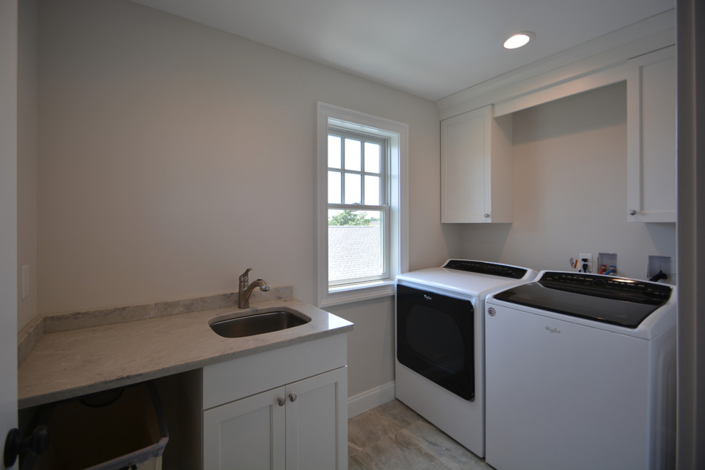 Example of a small beach style l-shaped porcelain tile and brown floor dedicated laundry room design in New York with an undermount sink, recessed-panel cabinets, white cabinets, granite countertops, beige walls, a side-by-side washer/dryer and beige countertops