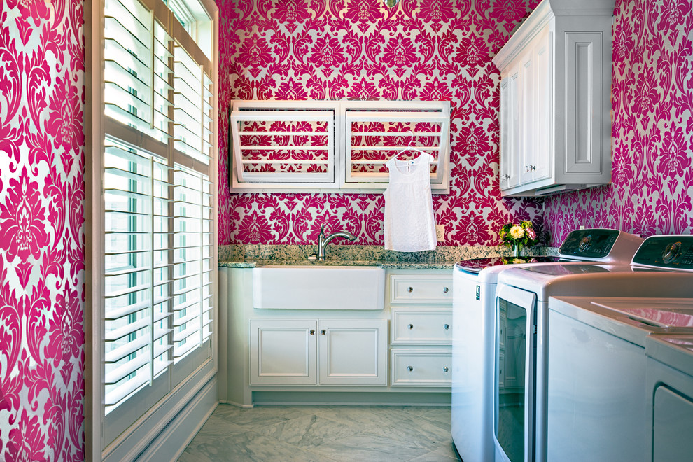 Inspiration for a mid-sized transitional l-shaped utility room remodel in Nashville with a farmhouse sink, recessed-panel cabinets, white cabinets, granite countertops, pink walls and a side-by-side washer/dryer