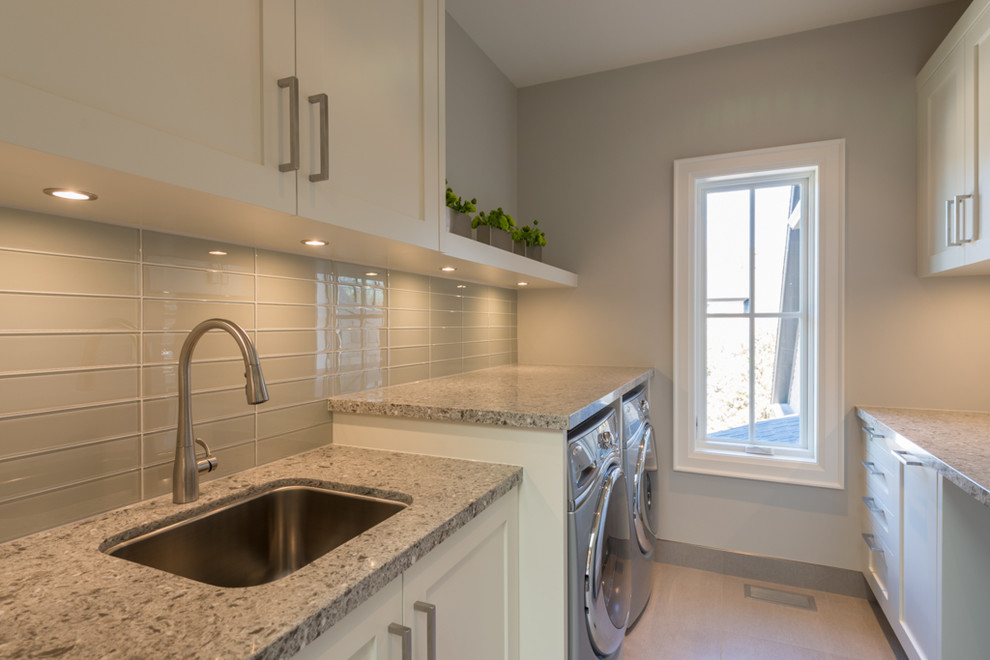Small galley separated utility room in Toronto with a submerged sink, shaker cabinets, white cabinets, composite countertops, grey walls, porcelain flooring and a side by side washer and dryer.